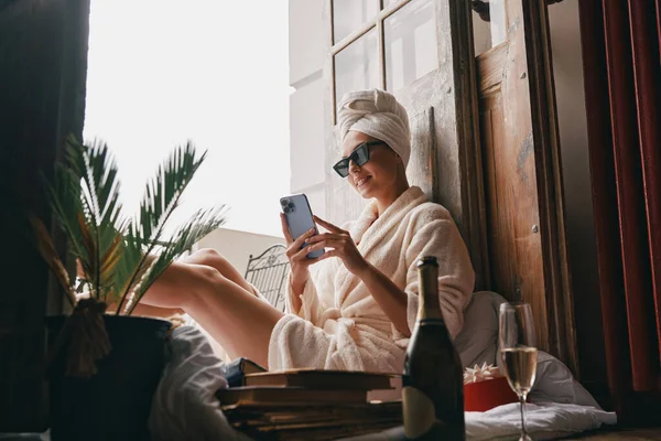 Hermosa Mujer Joven Albornoz Usando Teléfono Inteligente Mientras Está Sentada — Foto de Stock