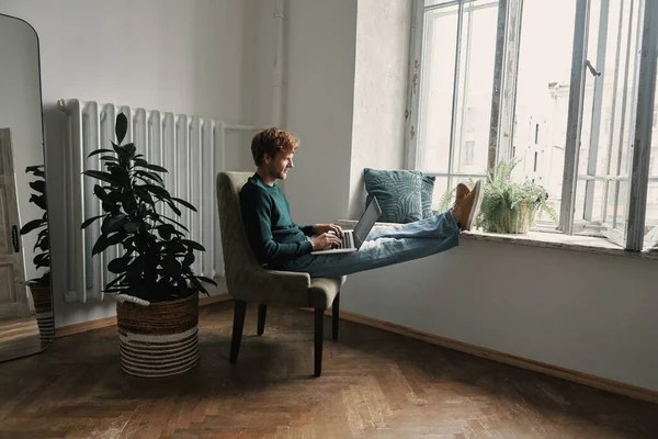Evdeki Sandalyede Otururken Dizüstü Bilgisayar Kullanan Kendine Güvenen Genç Adam — Stok fotoğraf