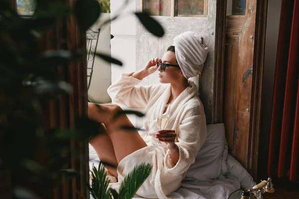 穿着浴衣的年轻貌美的女人一边在阳台上休息一边喝香槟 — 图库照片