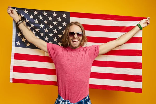 Szczęśliwy Młody Człowiek Niosący Amerykańską Flagę Stojąc Żółtym Tle — Zdjęcie stockowe