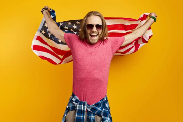 Podekscytowany Młody Człowiek Niosący Amerykańską Flagę Stojąc Żółtym Tle — Zdjęcie stockowe