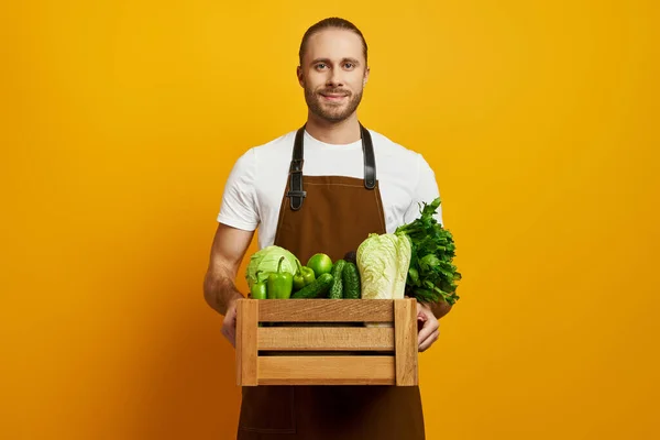 Confident Young Man Apron Carrying Wooden Crate Fresh Veggies Yellow — Stock Photo, Image