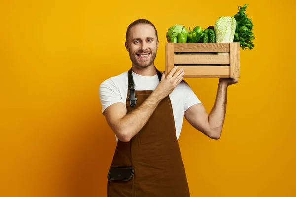 Happy Young Man Apron Carrying Wooden Crate Fresh Veggies Yellow — Stock Photo, Image