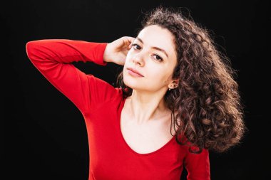 Kıvırcık saçlı genç bir kadın stüdyoda hayal gibi bir ifadeyle poz veriyor.