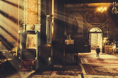 Bir otodoks kilisesinin içinde güneşli ışıklar ve tek başına duran bir çocuk.