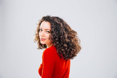 Kırmızı bluzlu, kıvırcık saçlı ve kameraya gülümseyen esmer bir kadının arka pozu.