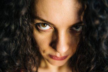 Kameraya bakan kıvırcık saçlı sinirli ciddi bir kadının portresi.