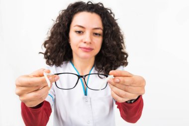 Kıvırcık saçlı, kameranın önünde gözlük tutan bir kadının bulanık duruşu. Gözlüklere odaklan, beyaza odaklan.. 