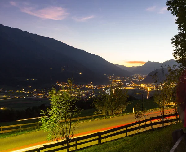 車の停止灯は日没時に道路上の連続線を作成します 長時間露光技術 背景にオーストリアの谷の光の街 — ストック写真