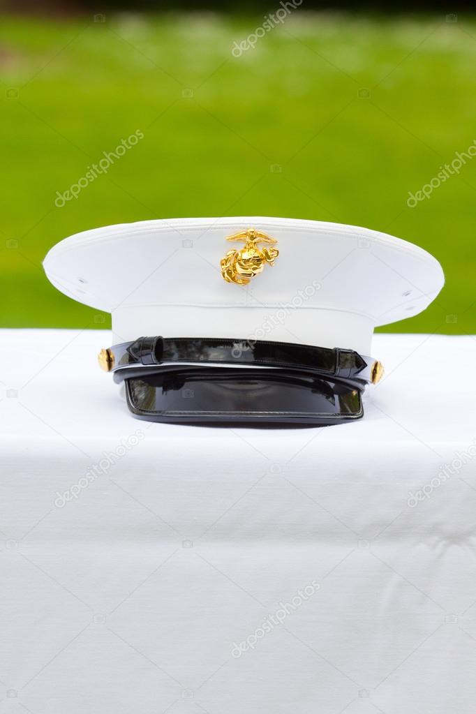 A marines hat off his head while at a wedding in uniform for armed forces soldiers and family.