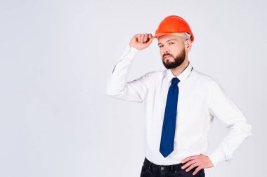 Olgun bir müteahhit, sakallı, miğferli, beyaz gömlekli ve kravatlı beyaz arka planda yalnız poz veriyor. Meslek, inşaat ve inşaat kavramı.