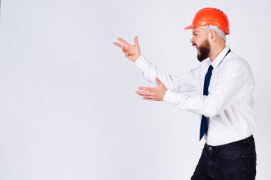 Etkileyici çığlıklar atan, agresif, olgun bir mimar, koruyucu bir miğfer takmış, izole beyaz bir arka planda, kızgın, yumruğunu sallayan, yana bakan bir adam. Kötü adam..