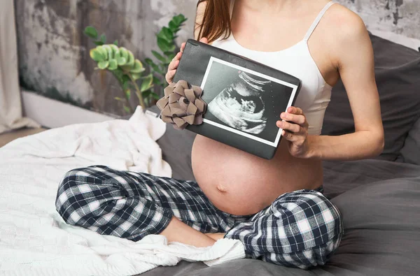 Close-up, Belly Of A Pregnant Young Girl Who Wears A Pink Sweater, Holds  White Headphones On Her Belly, The Baby Listens To Music. The Concept Of  Pregnancy, Motherhood, Preparation And Expectation. Stock