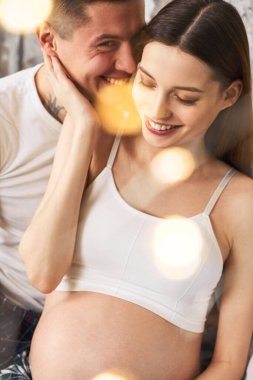 Yakın plan, pijamalı, yatakta aşık genç bir çift, birbirlerine sarılıp birlikte vakit geçiriyorlar. İlk çocuklarının doğumunu bekleyen genç bir çift..