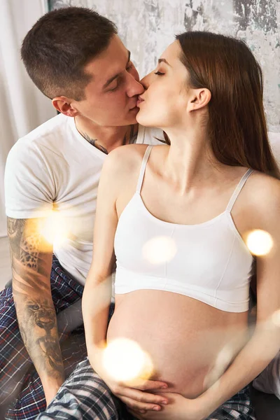 Dikey çekim, pijama giymiş genç ve evli bir çift öpüşüyor ve birlikte zaman geçiriyorlar. İlk çocuklarının doğumunu bekleyen genç bir çift..