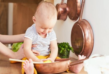 Tatlı beyaz bir oğlan, masada oturur, annesiyle bir tava ve limon oynar. Gerçek bir iç mekandaki günlük hayattan bir dizi fotoğraf..