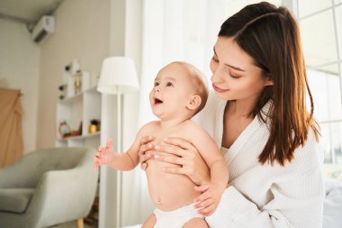 Mutlu genç anne, duştan sonra yeni doğmuş bebeğine bakıyor. Genç anne, küçük oğluna kucak dolusu sevgi ve özenle sarılıyor. Annelik ve evlat edinme kavramı, doğum sonrası dönemi..
