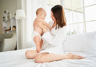 Sevgi dolu bir anne yeni doğmuş bebeğiyle evde oynar. Bebeğini kollarında tutan mutlu bir annenin portresi. Bir anne yatak odasında beyaz bir yatakta otururken oğluna sarılır. Çocukluk kavramı.