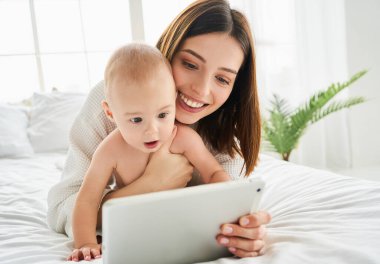 Beyaz, beyaz, yeni doğmuş bir bebek tablet üzerinde çizgi film izliyor. Küçük çocuk teknolojiyi kullanıyor. Eğitimin erken yaşta gelişmesi. Görüntülü konuşma, görüntülü arama.