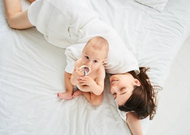 Beyaz tenli genç bir annenin bebeğiyle oynaması, yeni doğan oğlunun, sabah büyük bir yatakta yatması. Yalnız annelik ve çocukluk kavramı. Çocukların gelişimi, küçük çocuklar için oyuncaklar.