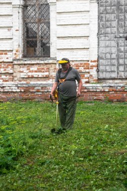 Bir adam müzenin bölgesindeki çimleri biçiyor.