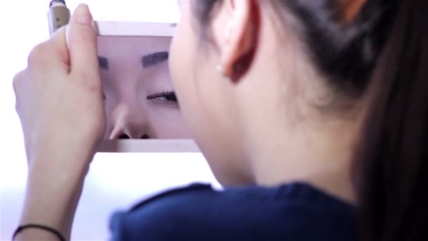 Young woman doing makeup in front of a mirror, full face, blurred background.Beautiful  young girl is doing makeup.Young woman with mirror and makeup brush. — Stock Video