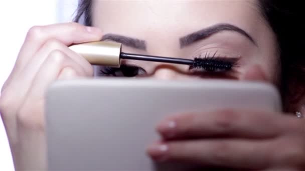 Молодая женщина делает макияж перед зеркалом, полное лицо, размытая спина. . — стоковое видео