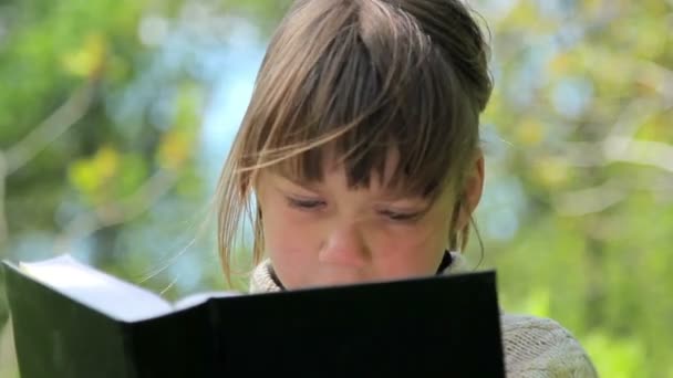 Junge liest ein Buch, Kind liest ein Buch im Park — Stockvideo