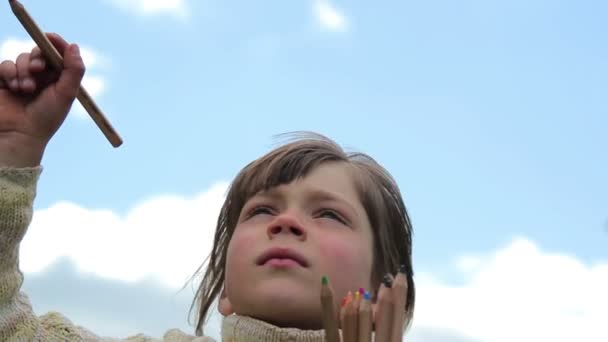 Мальчик с цветными карандашами, Ребенок с карандашами на фоне неба, краска в воздухе — стоковое видео
