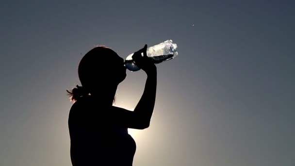 Mujer joven beber agua al atardecer. Chica bebe agua de una botella (bancos ) — Vídeos de Stock