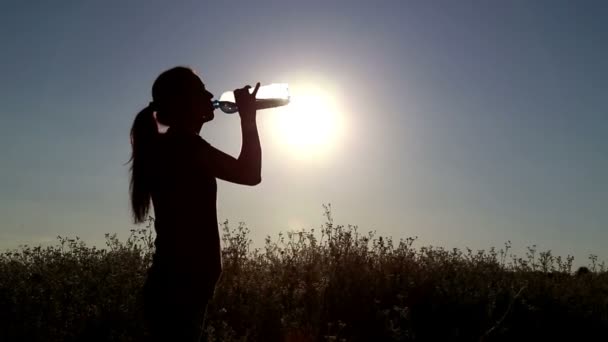 Νεαρή γυναίκα πίνουν νερό στο ηλιοβασίλεμα. Κορίτσι πίνει νερό από ένα μπουκάλι (τράπεζες) — Αρχείο Βίντεο
