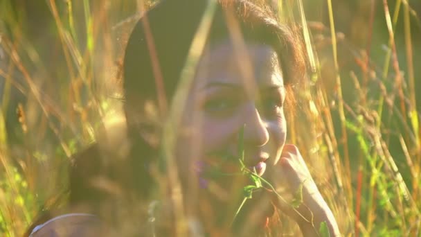 Retrato de una chica hermosa, sentada en la hierba. Niña en un campo al atardecer (retrato de cerca) ) — Vídeos de Stock
