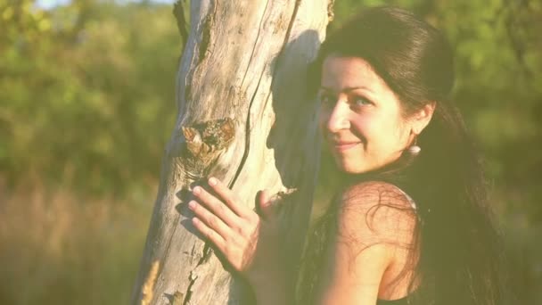 Hermosa chica en un parque, escondido detrás de un tronco de árbol.Hermosa, chica juguetona en la naturaleza . — Vídeo de stock