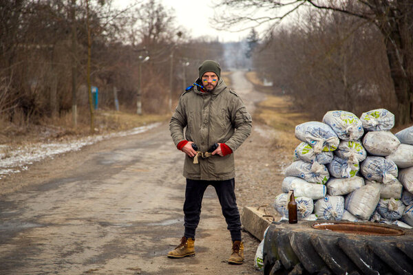 A Ukrainian man with a weapon at a checkpoint. A Ukrainian patriot guards the entrance to his village. 