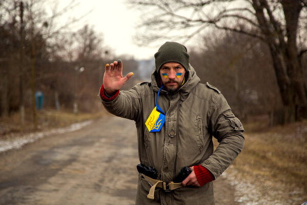 A Ukrainian man with a weapon at a checkpoint. A Ukrainian patriot guards the entrance to his village. 