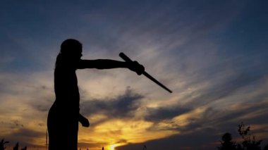 Gün batımında samuray kılıcıyla antrenman yapan bir çocuğun silueti. Samuray eğitimi kılıcıyla eskrim yapan genç bir çocuk.. 