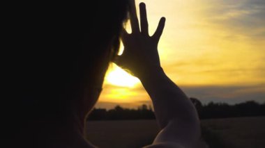 The girl stretches her hand to the sun at sunset standing on a country road. The sun at sunset shines through women's fingers. Dream and hope concept. 