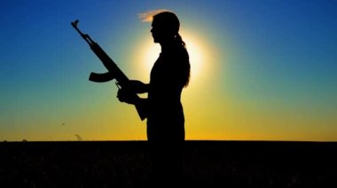 Ukrayna Savaşı. Tarlada Kalaşnikov saldırı tüfeği taşıyan genç bir adam. Kalaşnikof tüfekli bir adamın silueti. Savaş konsepti, terörizm, Ukrayna 'ya karşı saldırı. 