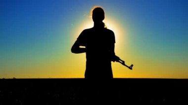 Ukrayna Savaşı. Tarlada Kalaşnikov saldırı tüfeği taşıyan genç bir adam. Kalaşnikof tüfekli bir adamın silueti. Savaş konsepti, terörizm, Ukrayna 'ya karşı saldırı. 
