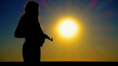The problem of sexism. A young boy-girl with a Kalashnikov assault rifle at sunset. A transgender man with a Kalashnikov in a field at dawn. The concept of justice, equality, sexual minorities, LGBT. 