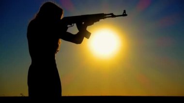 The problem of sexism. A young boy-girl with a Kalashnikov assault rifle at sunset. A transgender man with a Kalashnikov in a field at dawn. The concept of justice, equality, sexual minorities, LGBT. 