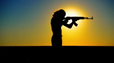 Ukrayna Savaşı. Tarlada Kalaşnikov saldırı tüfeği taşıyan genç bir adam. Kalaşnikof tüfekli bir adamın silueti. Savaş konsepti, terörizm, Ukrayna 'ya karşı saldırı. 