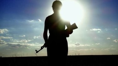 Ukrayna Savaşı. Kalaşnikof tüfekli genç bir kadın sahada eğitim görüyor. Kalaşnikof tüfekli bir kızın silueti. Savaş konsepti, terörizm, Ukrayna 'ya karşı saldırı. 