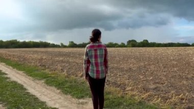 Lonely young woman on a rural road. The girl stands, walks, runs along the village road before the rain. The concept of loneliness, hopelessness. 