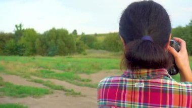 A young woman in a field photographs nature. A girl with a camera walks in nature. Camera movement towards the subject. The concept of happiness, hobby, relaxation. 