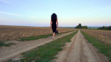 A beautiful young woman walks with a Staffordshire Terrier in a field. Happy free girl on a walk with a dog in nature. The concept of happiness, freedom, pets. 