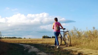 Young happy woman on a bike in the field. Girl rides a bike in nature. Close-up portrait, view from behind the grass. Camera movement.Concept of happiness, recreation, sports, nature. 