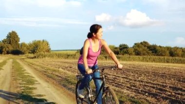 Young happy woman on a bike in the field. Girl rides a bike in nature. Close-up portrait, view from behind the grass. Camera movement.Concept of happiness, recreation, sports, nature. 