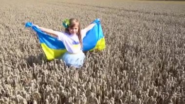 Little girl with the Ukrainian flag in the field. Child girl with the flag of Ukraine in the field of wheat. The concept of freedom, independence, peace. 