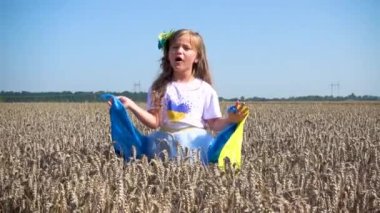 Little girl with the Ukrainian flag in the field. Child girl with the flag of Ukraine in the field of wheat. The concept of freedom, independence, peace. 